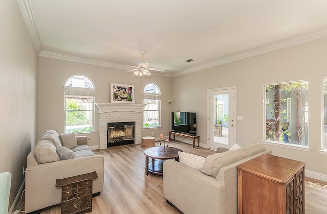living room featuring crown molding, ceiling fan, light wood-style flooring, a brick fireplace, and baseboards