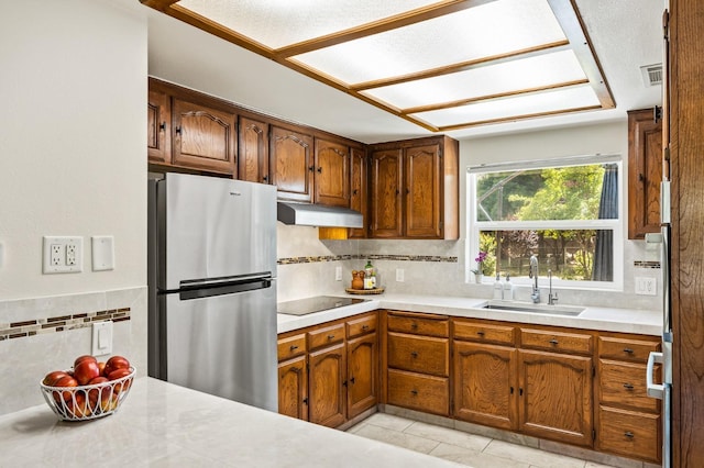 13801 E Rialto Ave, Sanger, CA 93657 - kitchen with freestanding refrigerator, a sink, black electric stovetop, under cabinet range hood, and decorative backsplash