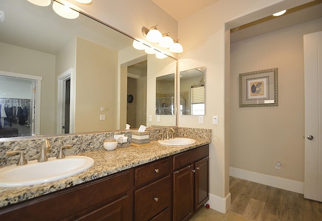 full bathroom featuring double vanity, wood finished floors, baseboards, and a shower