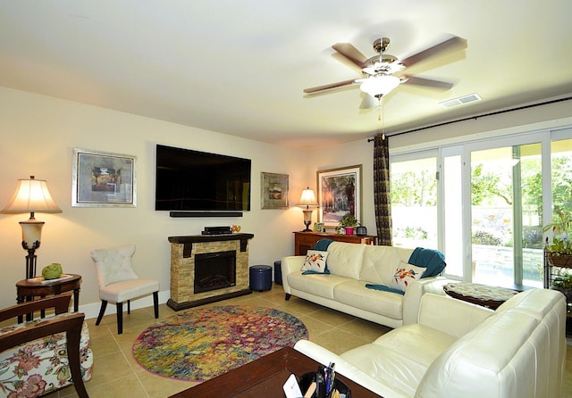 living room featuring light tile patterned floors, ceiling fan, and a stone fireplace