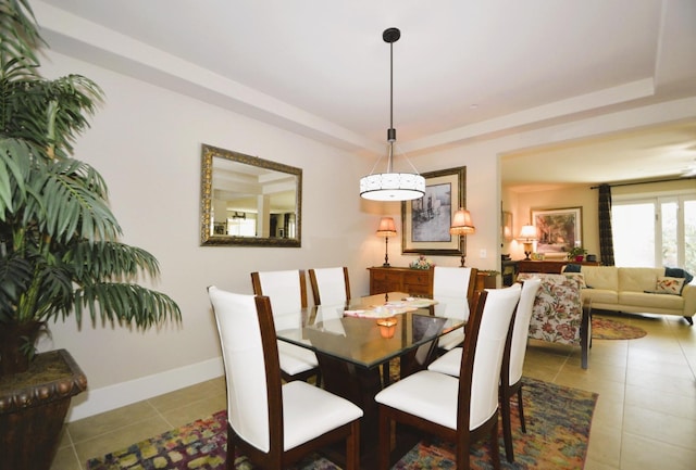 tiled dining area with a tray ceiling and baseboards