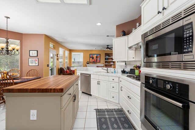 kitchen featuring stainless steel appliances, wooden counters, a chandelier, a peninsula, and light tile patterned floors