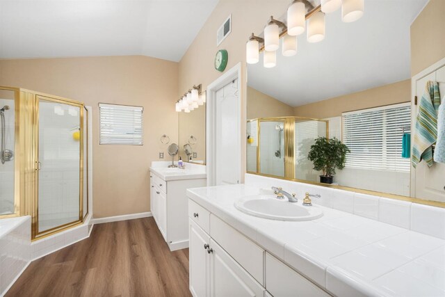 bathroom with lofted ceiling, wood finished floors, a stall shower, and two vanities