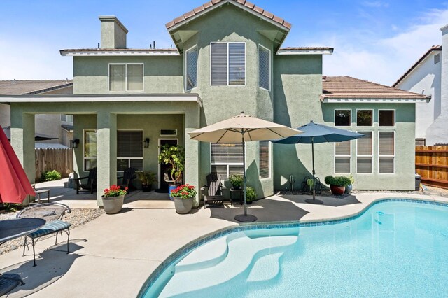 back of property with a patio area, fence, stucco siding, an outdoor pool, and a chimney