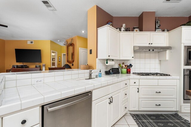 kitchen featuring stainless steel appliances, under cabinet range hood, a sink, tile countertops, and tasteful backsplash