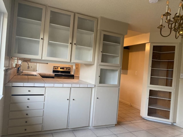 kitchen with a sink, tile counters, electric stove, light tile patterned flooring, and a chandelier