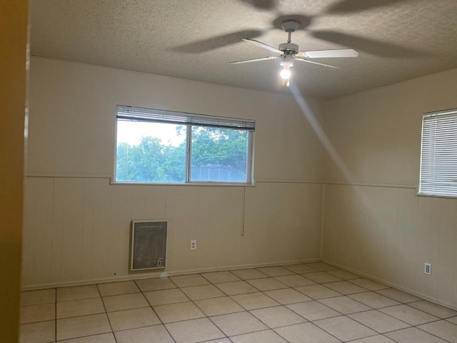 spare room featuring a textured ceiling, a ceiling fan, light tile patterned floors, a wainscoted wall, and baseboards