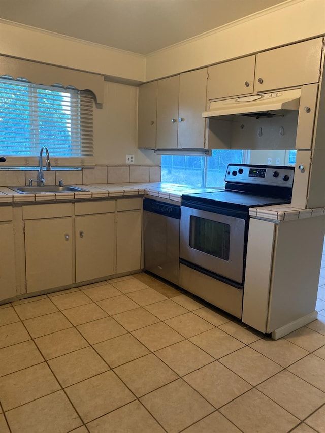 kitchen featuring appliances with stainless steel finishes, a sink, tile counters, ornamental molding, and light tile patterned flooring