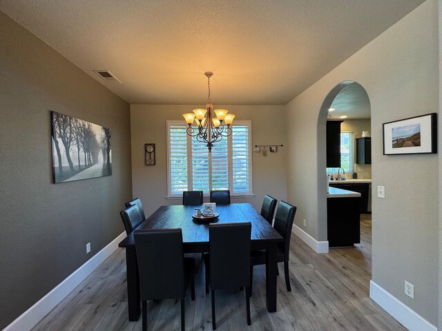 1822 N Magnolia, Clovis, CA 93619 - dining room with light wood-type flooring, a chandelier, arched walkways, baseboards, and a textured ceiling