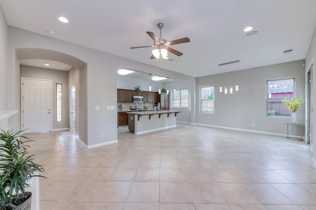 unfurnished living room with arched walkways, a ceiling fan, light tile patterned floors, recessed lighting, and baseboards