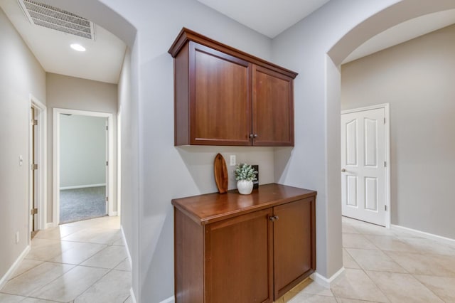 hallway featuring arched walkways, light tile patterned floors, baseboards, and recessed lighting