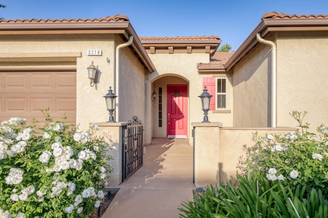 property entrance with stucco siding, an attached garage, a gate, and fence