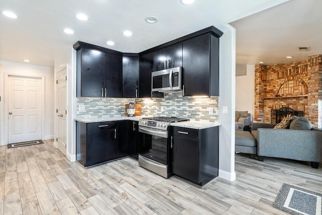 2371 Sophia Ln, Kingsburg, CA 93631 - kitchen with stainless steel appliances, dark cabinetry, decorative backsplash, light wood-style flooring, and recessed lighting