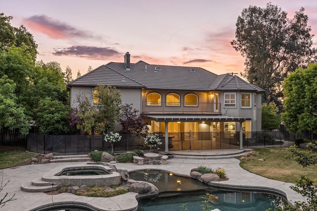 2758 N Highland Ave, Fresno, CA 93737 - back of property at dusk with an in-ground hot tub, a balcony, fence, a chimney, and a patio area