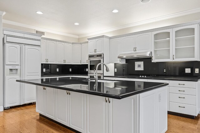 2758 N Highland Ave, Fresno, CA 93737 - kitchen featuring paneled built in fridge, under cabinet range hood, dark countertops, crown molding, and glass insert cabinets