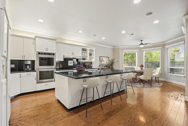 2758 N Highland Ave, Fresno, CA 93737 - kitchen with double oven, a breakfast bar, crown molding, a center island with sink, and dark countertops