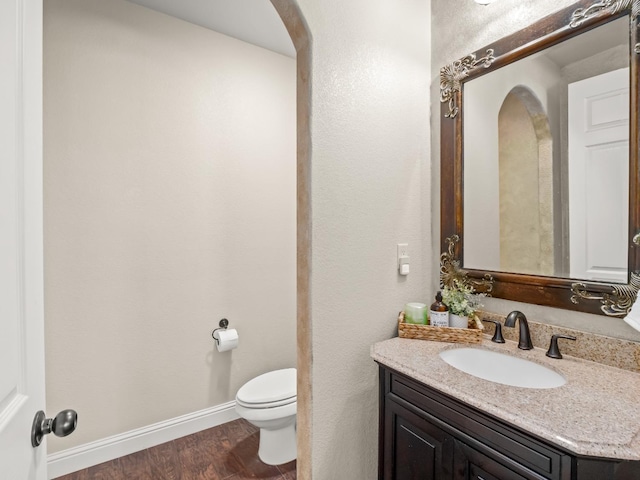 bathroom with toilet, wood finished floors, vanity, and baseboards