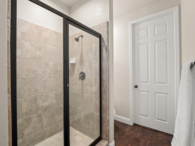 bathroom featuring wood finished floors, a stall shower, baseboards, and toilet