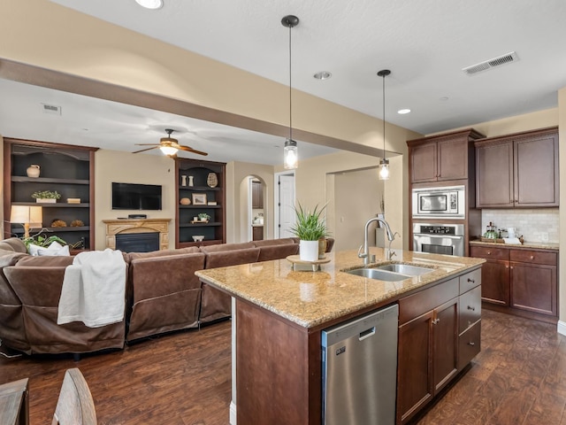 kitchen featuring appliances with stainless steel finishes, a sink, open floor plan, dark wood-type flooring, and a fireplace
