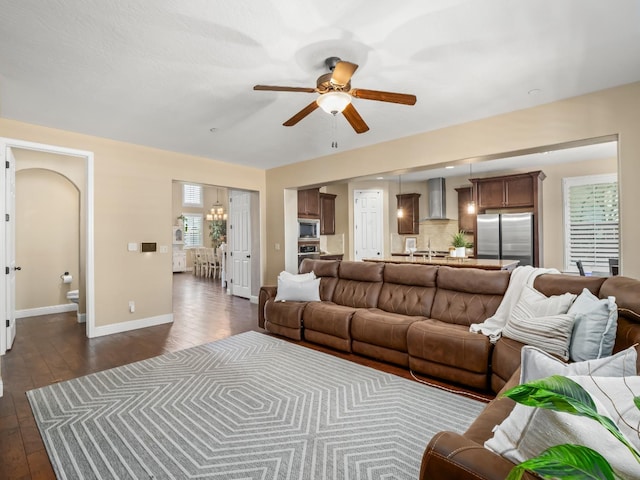 living area with a ceiling fan, dark wood-style flooring, baseboards, and a chandelier