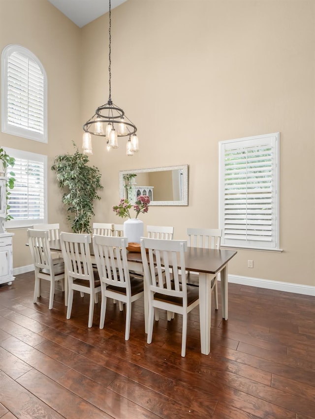 dining room featuring a towering ceiling, dark wood-style floors, a chandelier, and baseboards