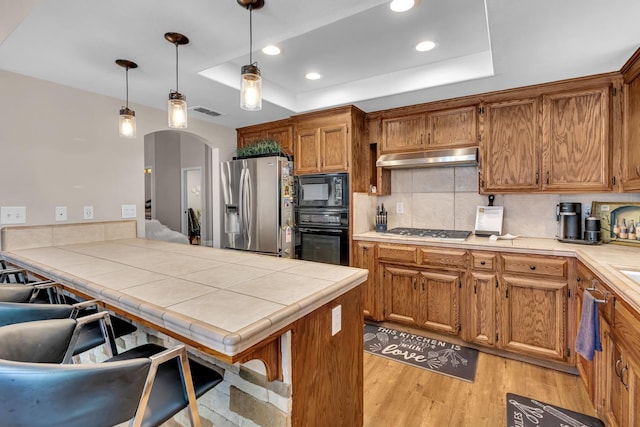 22 Pointe W, Madera, CA 93637 - kitchen featuring black appliances, a tray ceiling, arched walkways, light wood-type flooring, and tasteful backsplash
