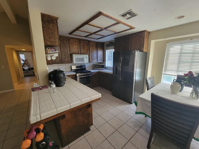 5566 W Fir Ave, Fresno, CA 93722 - kitchen with stainless steel appliances, tile countertops, light tile patterned flooring, dark brown cabinetry, and tasteful backsplash
