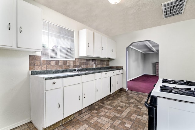 kitchen with range with gas stovetop, arched walkways, white cabinetry, and baseboards