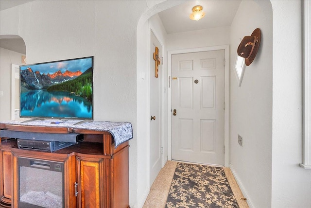 foyer with arched walkways, light carpet, and baseboards