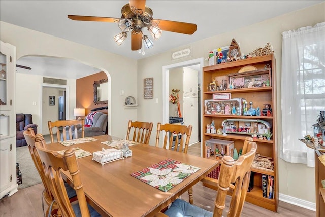 dining area featuring arched walkways, a ceiling fan, and light wood-style floors