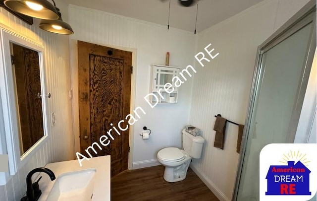bathroom with wood finished floors, toilet, a sink, baseboards, and crown molding
