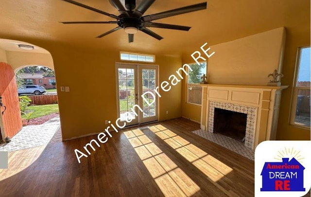 unfurnished living room featuring wood finished floors, a fireplace, ceiling fan, and arched walkways