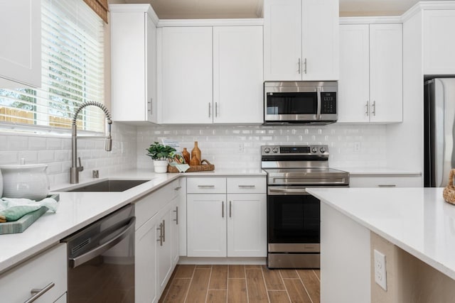 kitchen with stainless steel appliances, a sink, white cabinetry, and light wood-style flooring