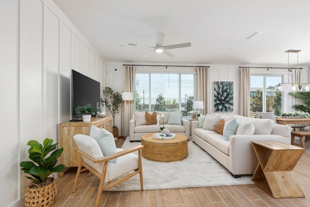 living room featuring light wood-type flooring, ceiling fan, and a decorative wall