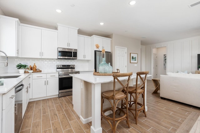 kitchen with appliances with stainless steel finishes, a sink, wood tiled floors, a kitchen island, and backsplash