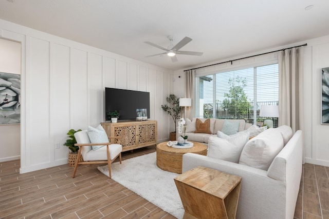 living area with wood finished floors, a ceiling fan, a decorative wall, and baseboards
