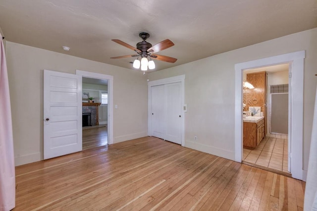 unfurnished bedroom featuring light wood-style floors, baseboards, a fireplace, a closet, and a ceiling fan