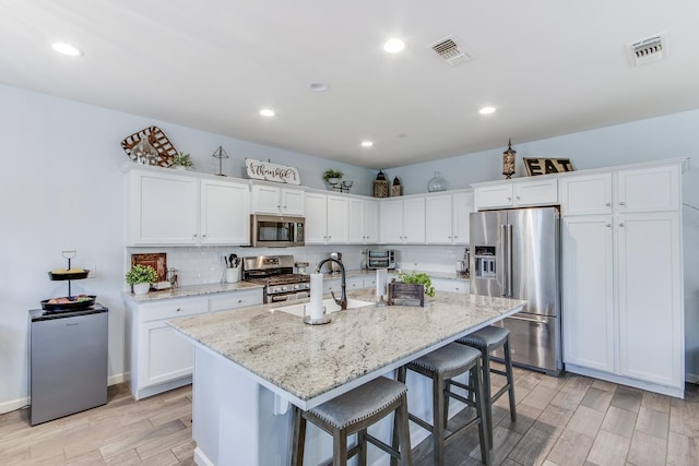 3877 Griffith Ave, Clovis, CA 93619 - kitchen with appliances with stainless steel finishes, a sink, light wood-style floors, a kitchen breakfast bar, and white cabinetry