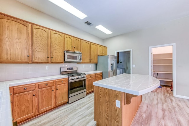 947 Carson Ave, Clovis, CA 93611 - kitchen with appliances with stainless steel finishes, light wood finished floors, a kitchen island, tile counters, and tasteful backsplash