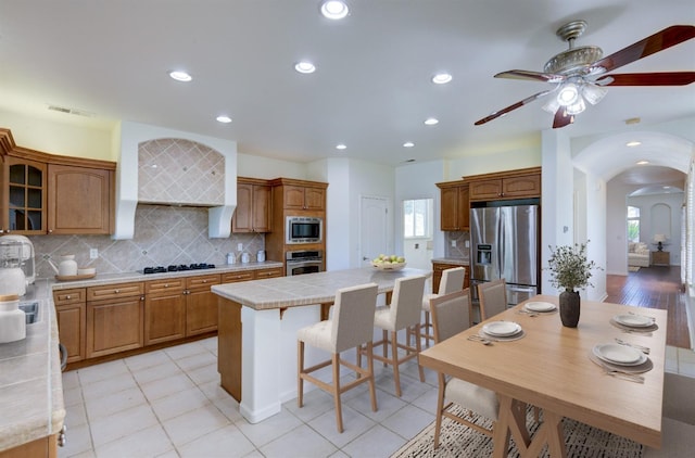 30925 Pennyroyal Ln, Prather, CA 93651 - kitchen featuring stainless steel appliances, a center island, arched walkways, a ceiling fan, and backsplash