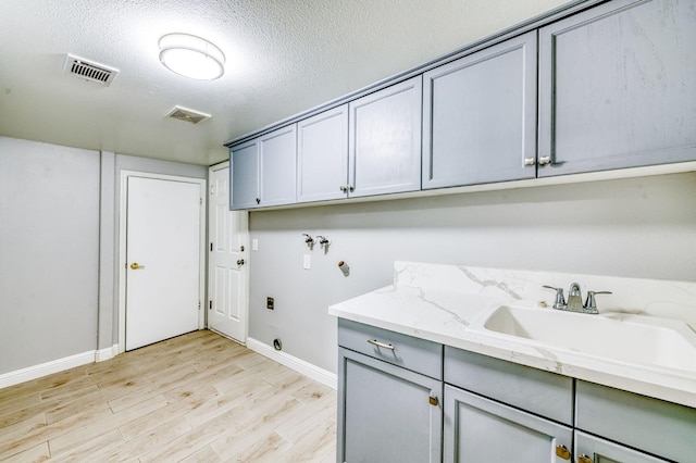 clothes washing area featuring washer hookup, cabinet space, baseboards, light wood-style floors, and a textured ceiling
