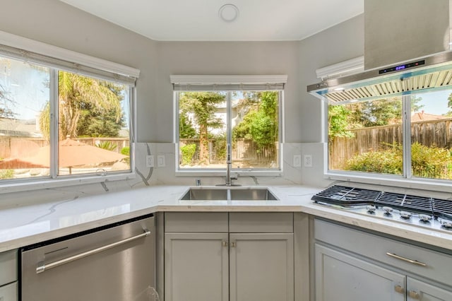 kitchen featuring appliances with stainless steel finishes, wall chimney exhaust hood, a sink, light stone counters, and decorative backsplash
