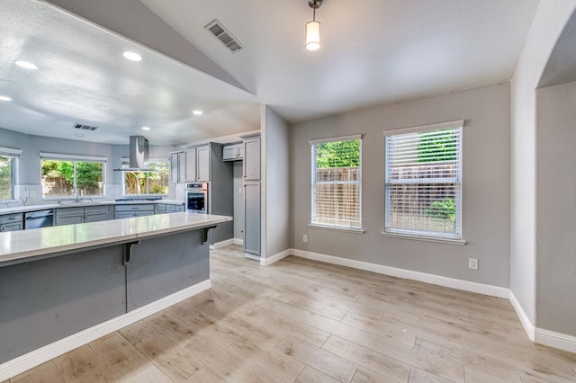 kitchen with island exhaust hood, appliances with stainless steel finishes, light countertops, vaulted ceiling, and a sink