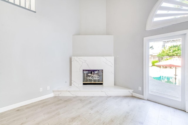 unfurnished living room featuring wood finished floors, baseboards, a fireplace, and a towering ceiling