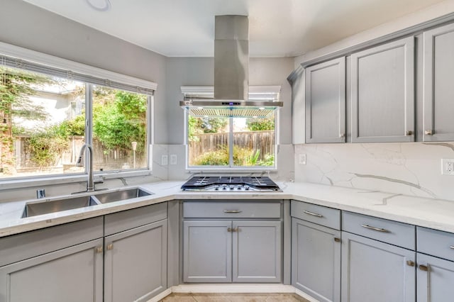 kitchen featuring gray cabinetry, a sink, stainless steel gas cooktop, and island exhaust hood