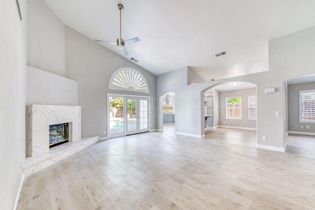 unfurnished living room featuring a ceiling fan, a premium fireplace, arched walkways, baseboards, and high vaulted ceiling