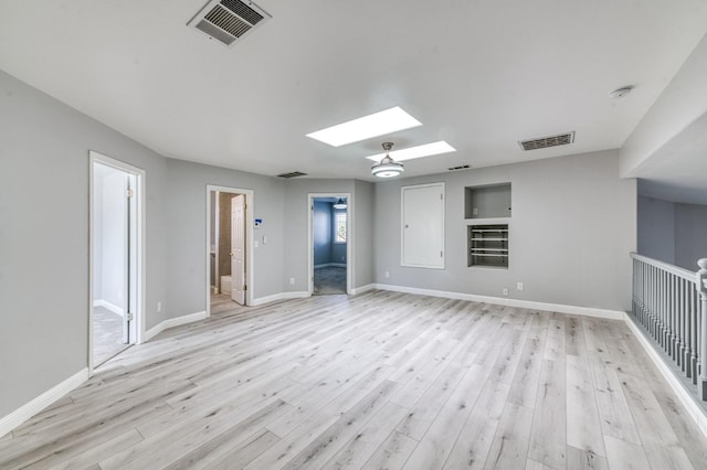 unfurnished room featuring a skylight, light wood-type flooring, a smoke detector, and baseboards