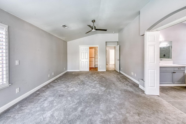 unfurnished bedroom featuring lofted ceiling, carpet flooring, baseboards, ensuite bathroom, and a spacious closet