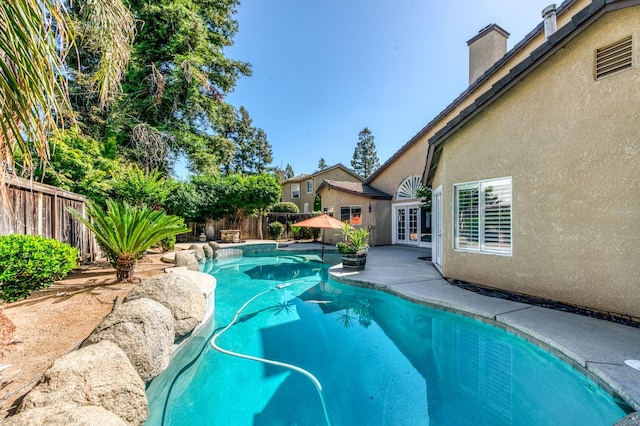 view of pool with french doors, a fenced backyard, and a patio