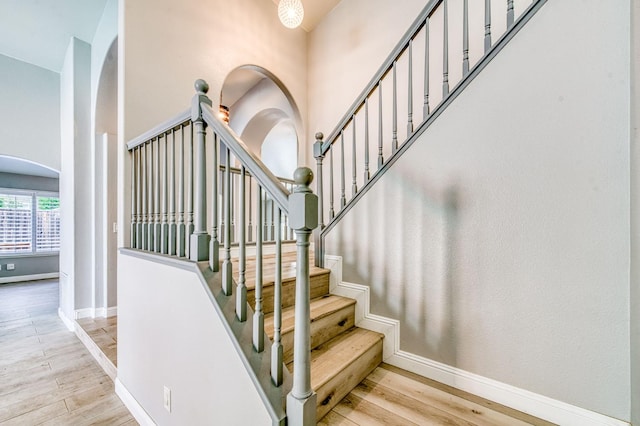staircase featuring wood finished floors, arched walkways, baseboards, and a high ceiling